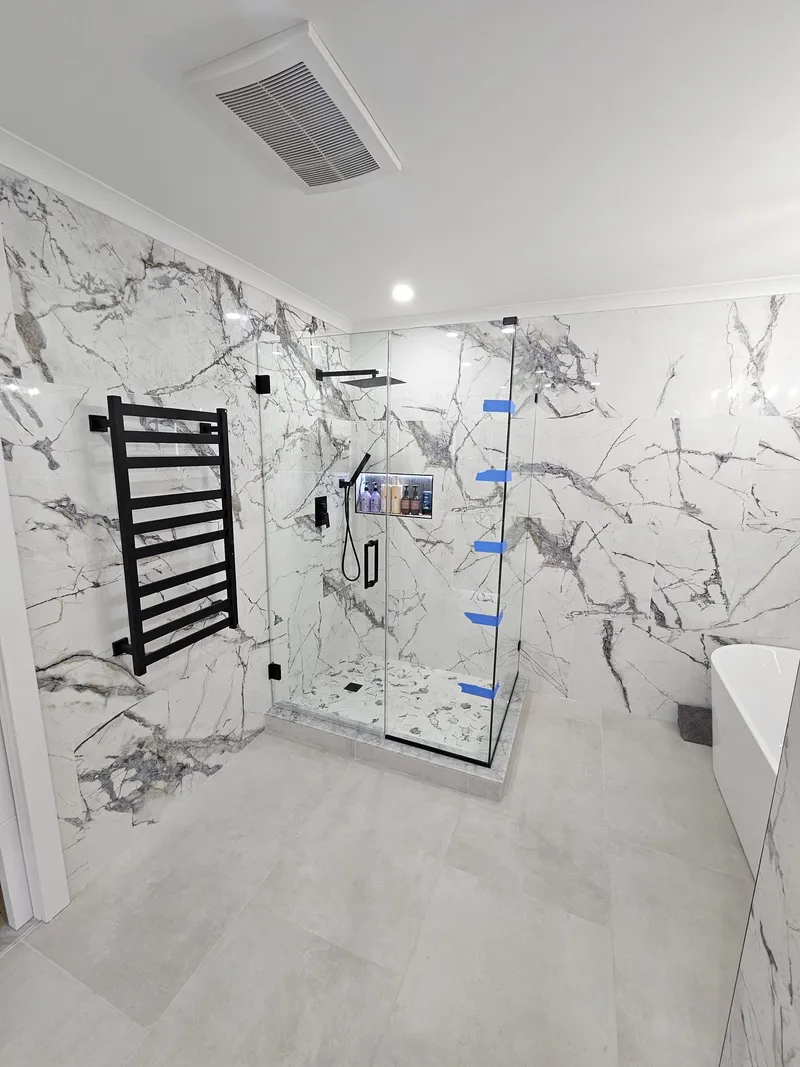 A walk-in shower in book-matched marble tile with a black towel warmer beside it