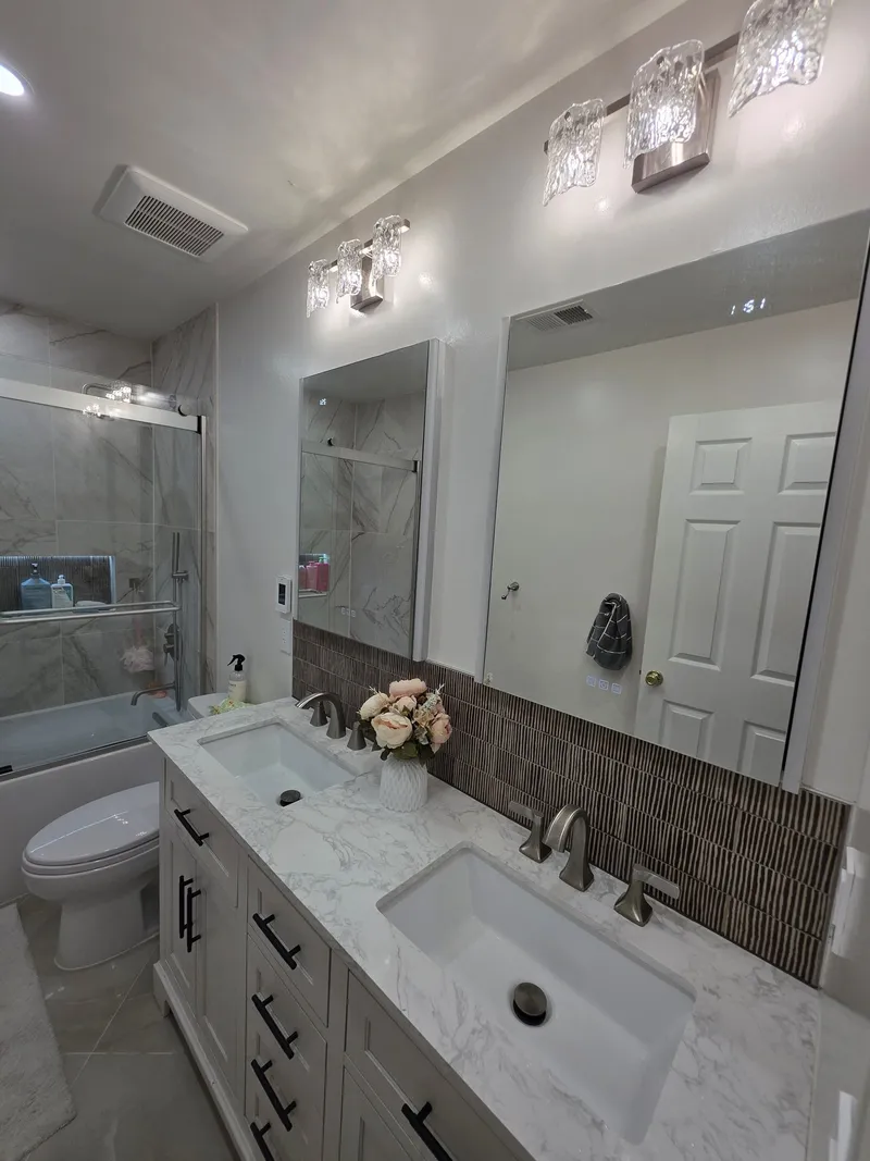 A double vanity with a marble-look countertop, a wide mirror and a lit shower niche behind