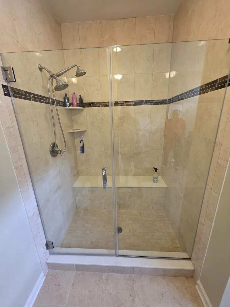 A travertine shower with a framed glass door and a mosaic accent band