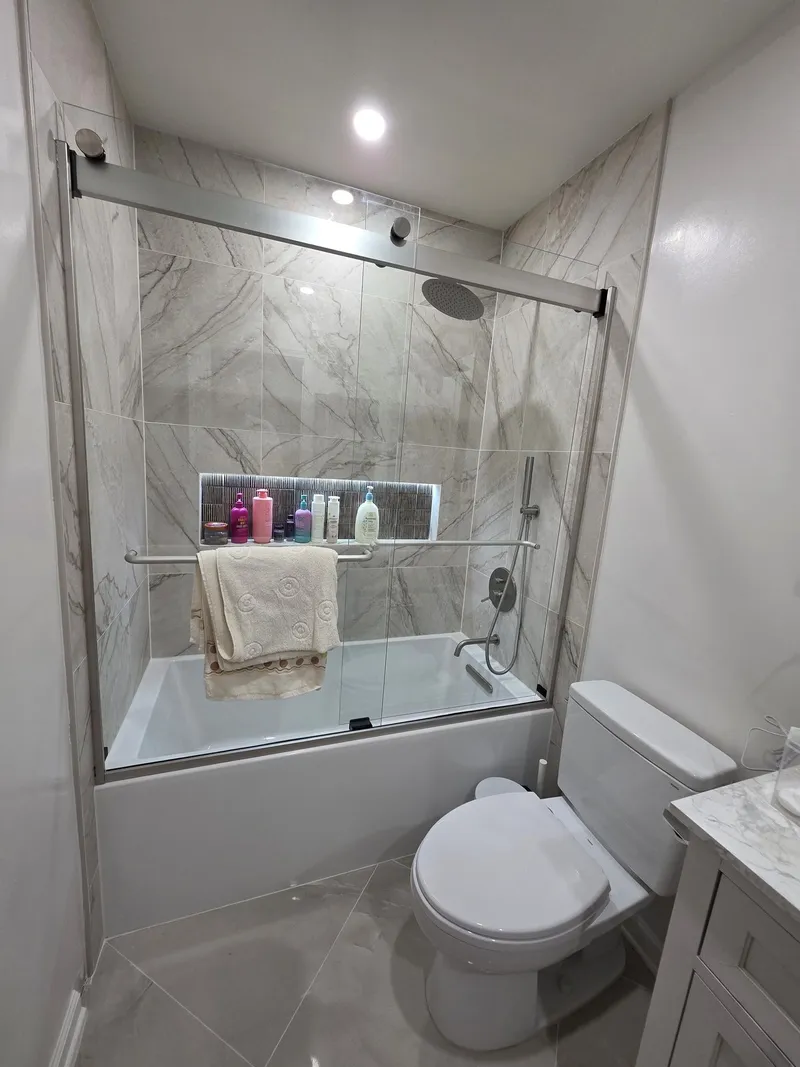 A tub-and-shower combination with marble-look tile, a niche and a sliding glass door
