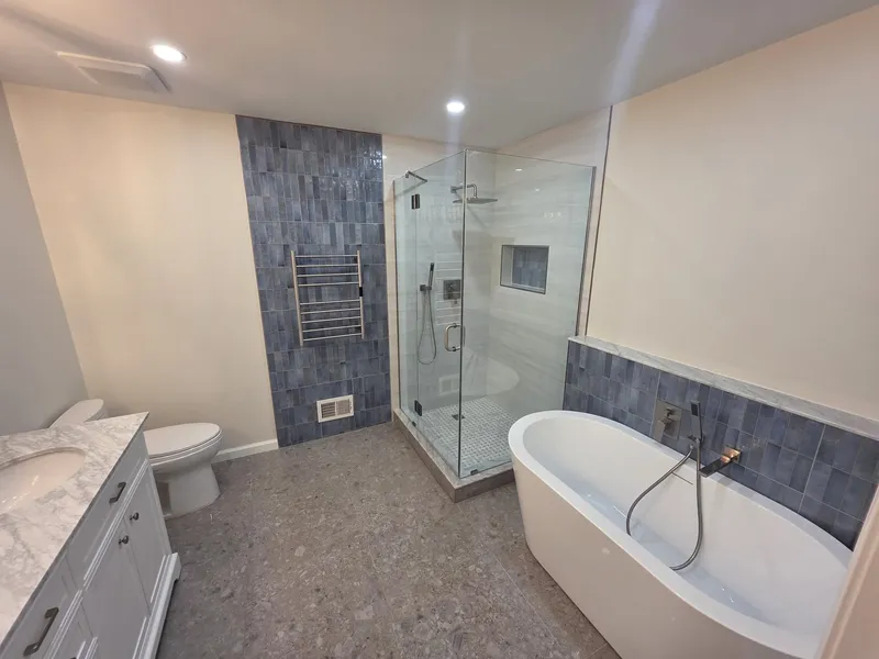 A finished bathroom with a freestanding tub, a frameless glass shower and blue-grey feature tile