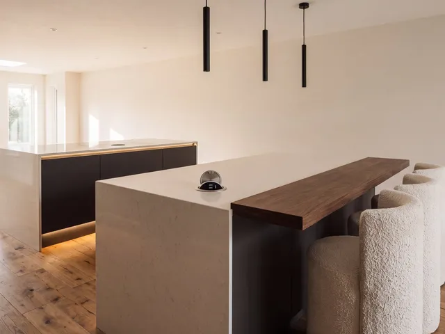 A quartz waterfall island with pendant lights, a walnut breakfast bar and a pop-up charging outlet open in the counter