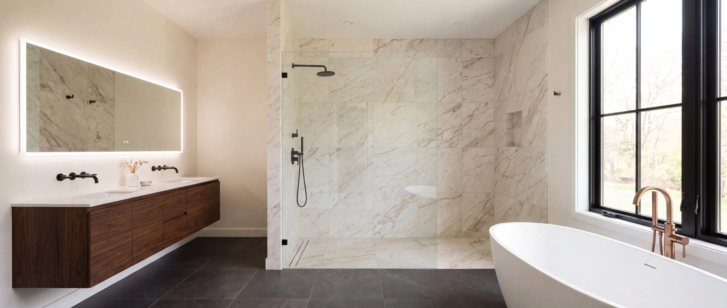 A primary bathroom in warm stone, walnut and matte black, built to the TrueLevel standard