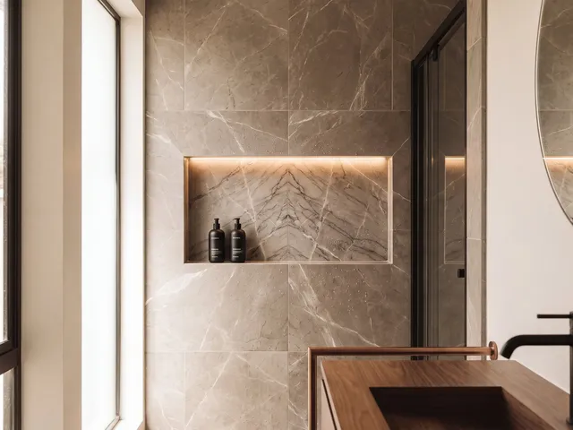 A recessed marble shower niche with a book-matched back panel and a thin warm LED strip along its top edge