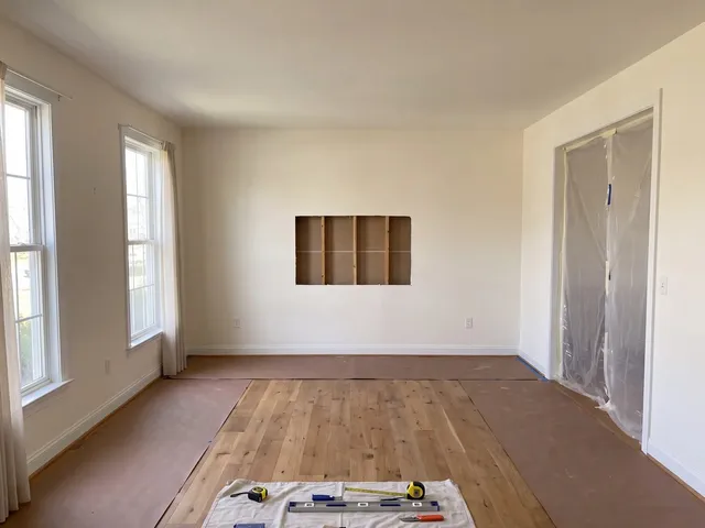 A living room stripped for work with the floor covered and an opening cut into the wall